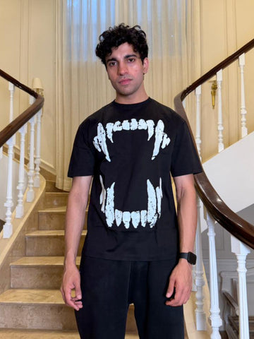 Person wearing a black t-shirt with white graphics in a home setting with stairs and railings.